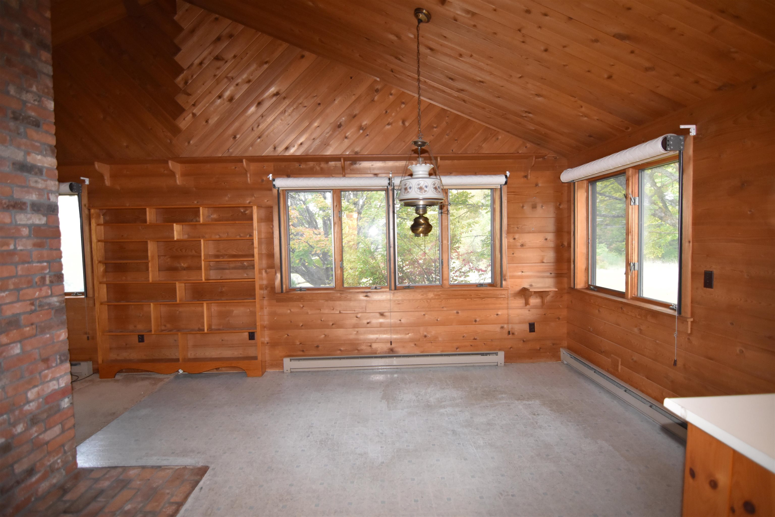 Wood-paneled room with a vaulted ceiling, built-in shelves, brick fireplace, and large windows.