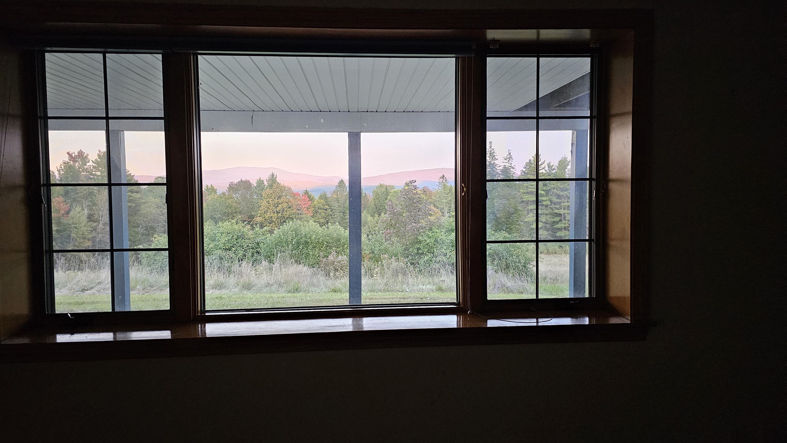 Wide wood-framed windows overlook autumn trees and distant mountain ridges.
