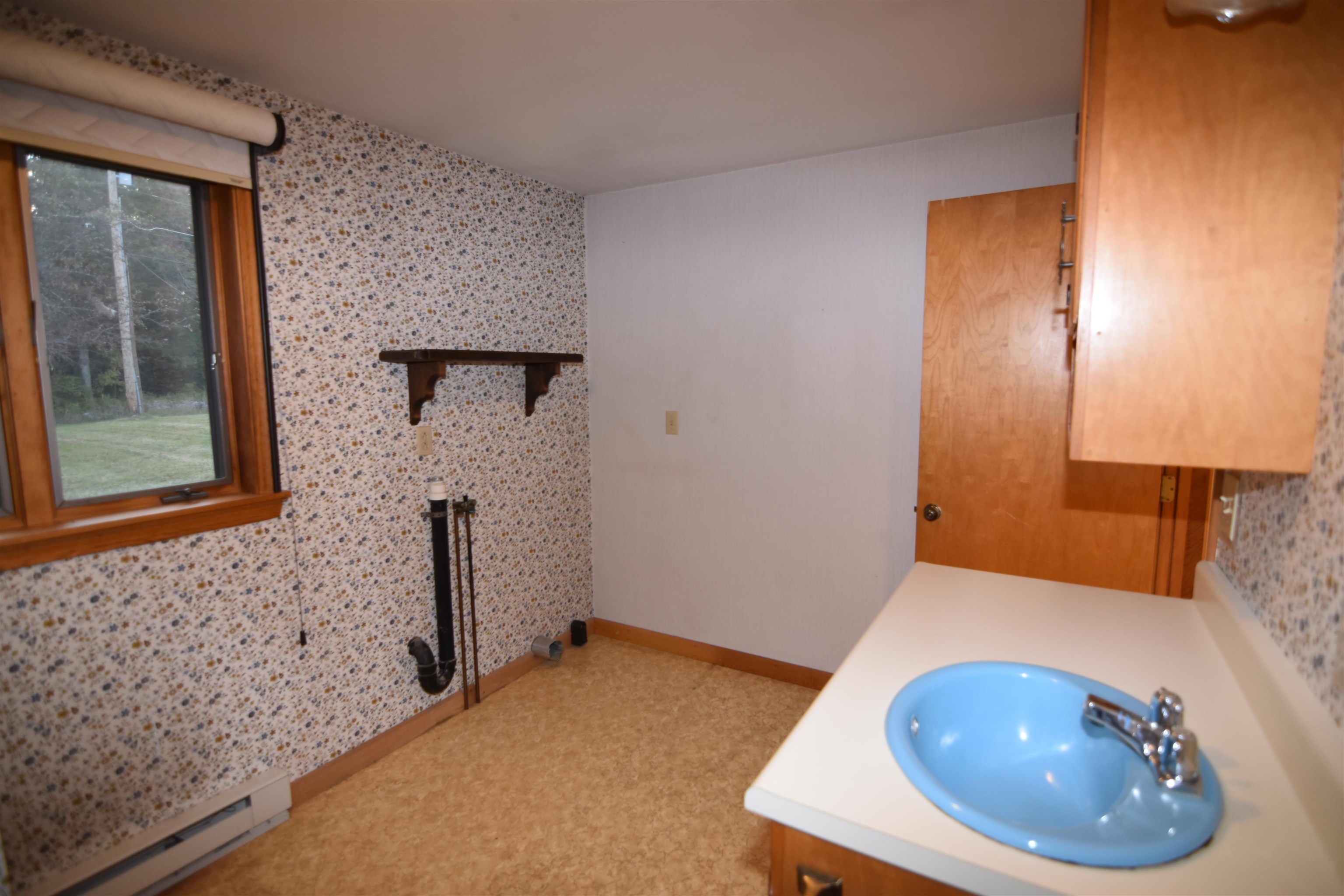 Bathroom with a bright blue vanity sink, wood cabinetry, and floral wallpaper.