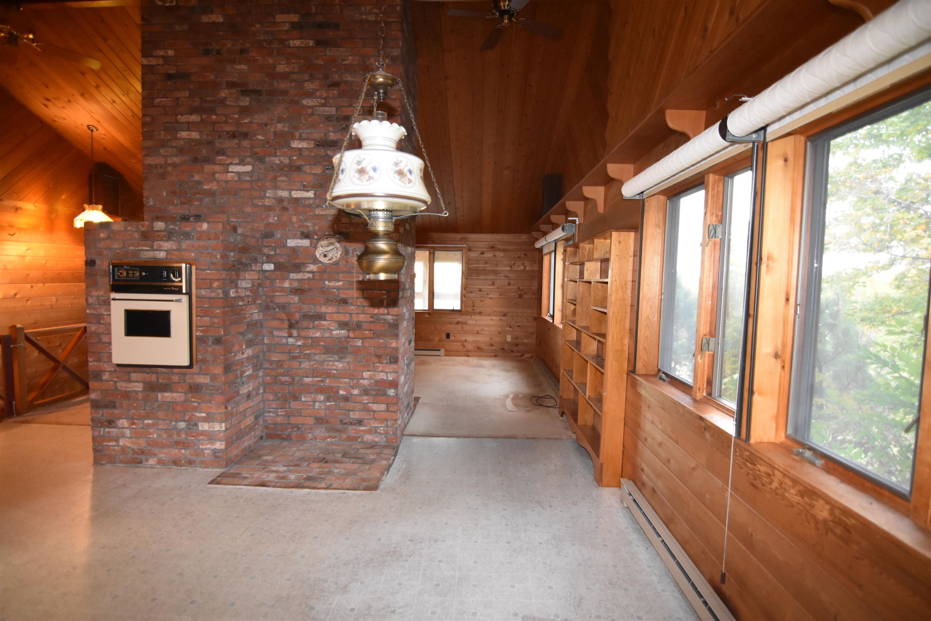 Wood-paneled room with a brick chimney, built-in oven, long windows, and open shelving.