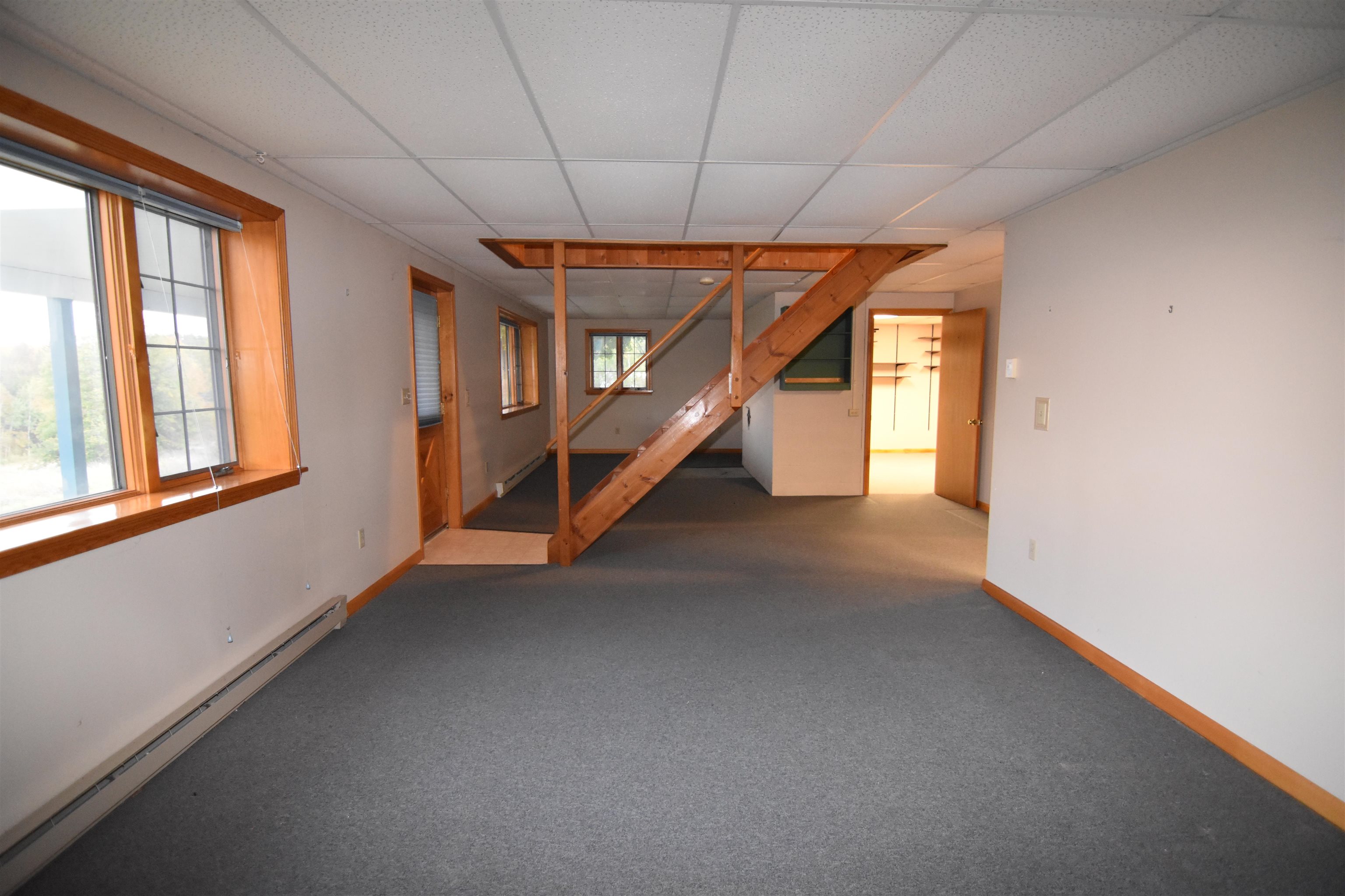 Vacant carpeted room with wood-trimmed windows and an exposed wooden staircase.