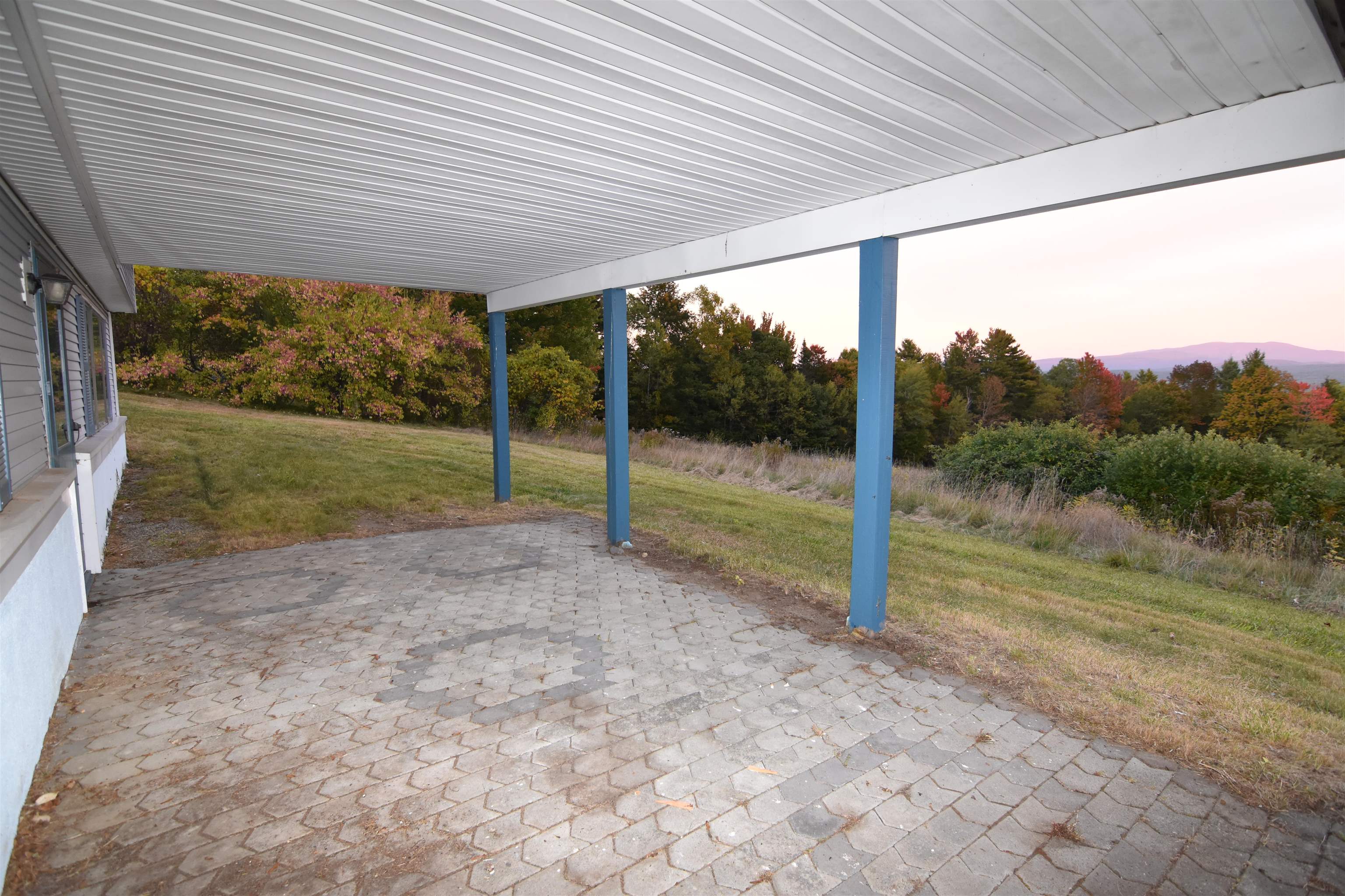 Covered paver patio with blue posts overlooks an autumn hillside and distant mountains.