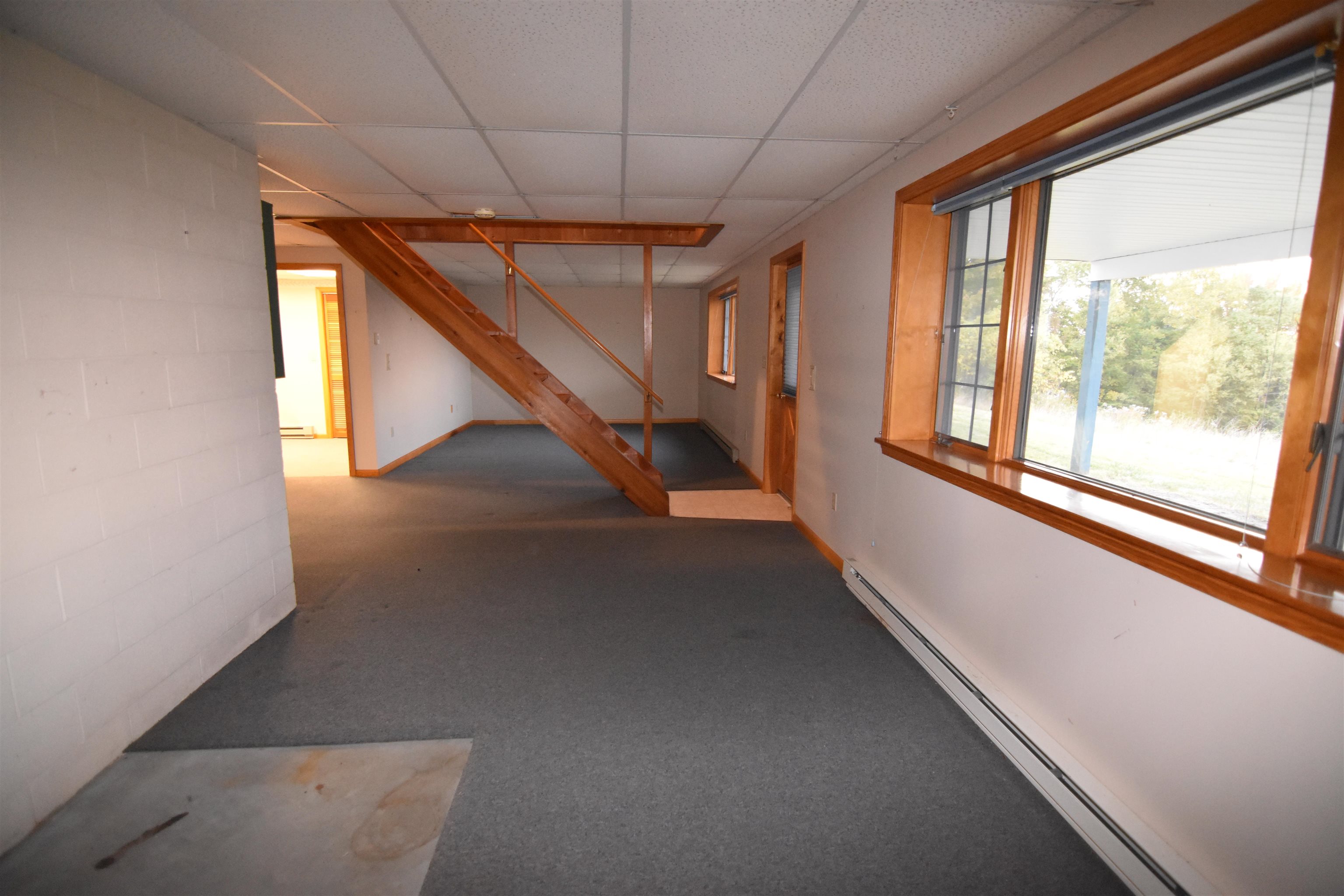 Vacant carpeted room with a wooden staircase and large wood-trimmed window.