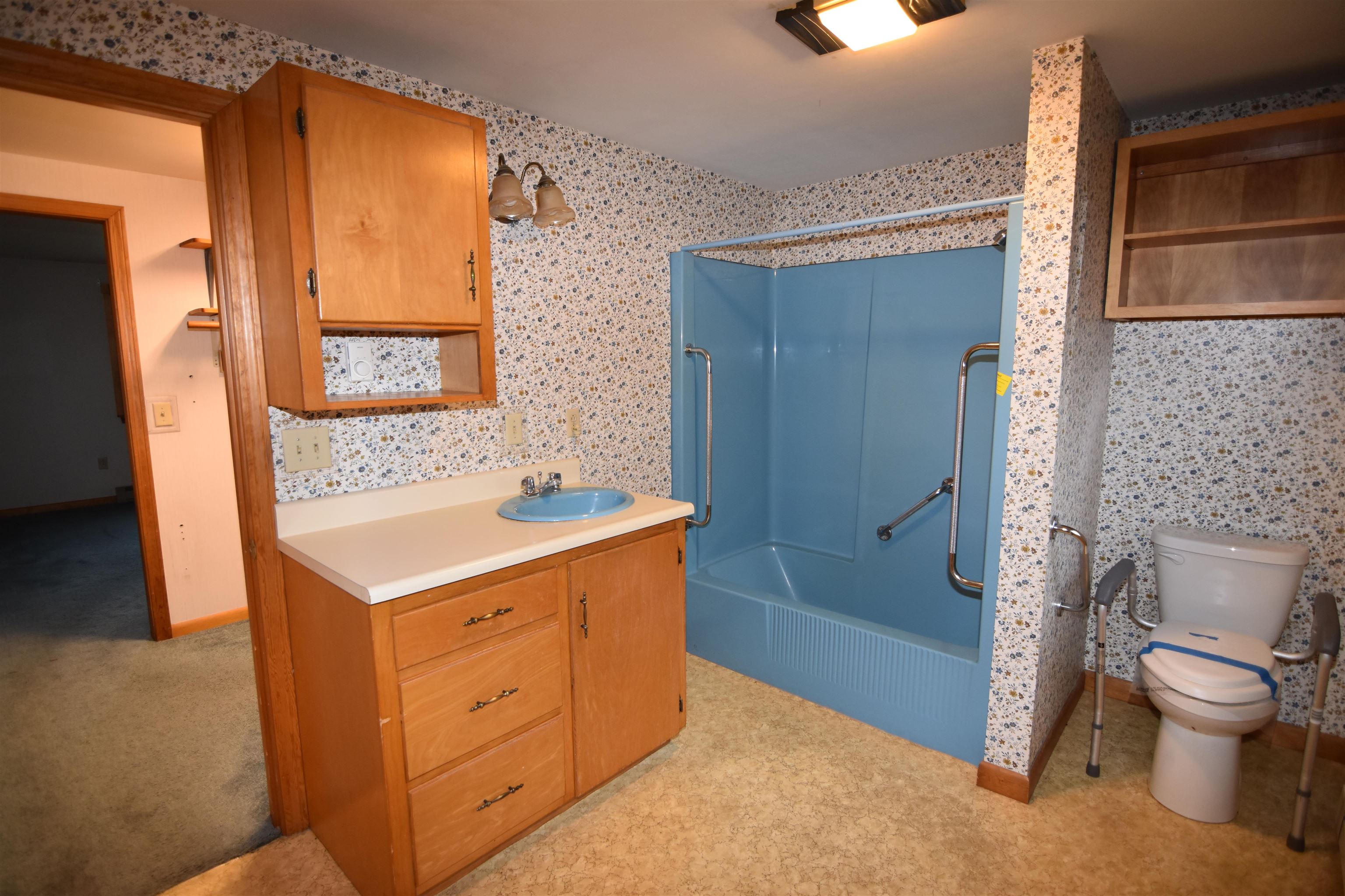 Bathroom with a blue accessible shower, grab bars, and a wooden vanity.