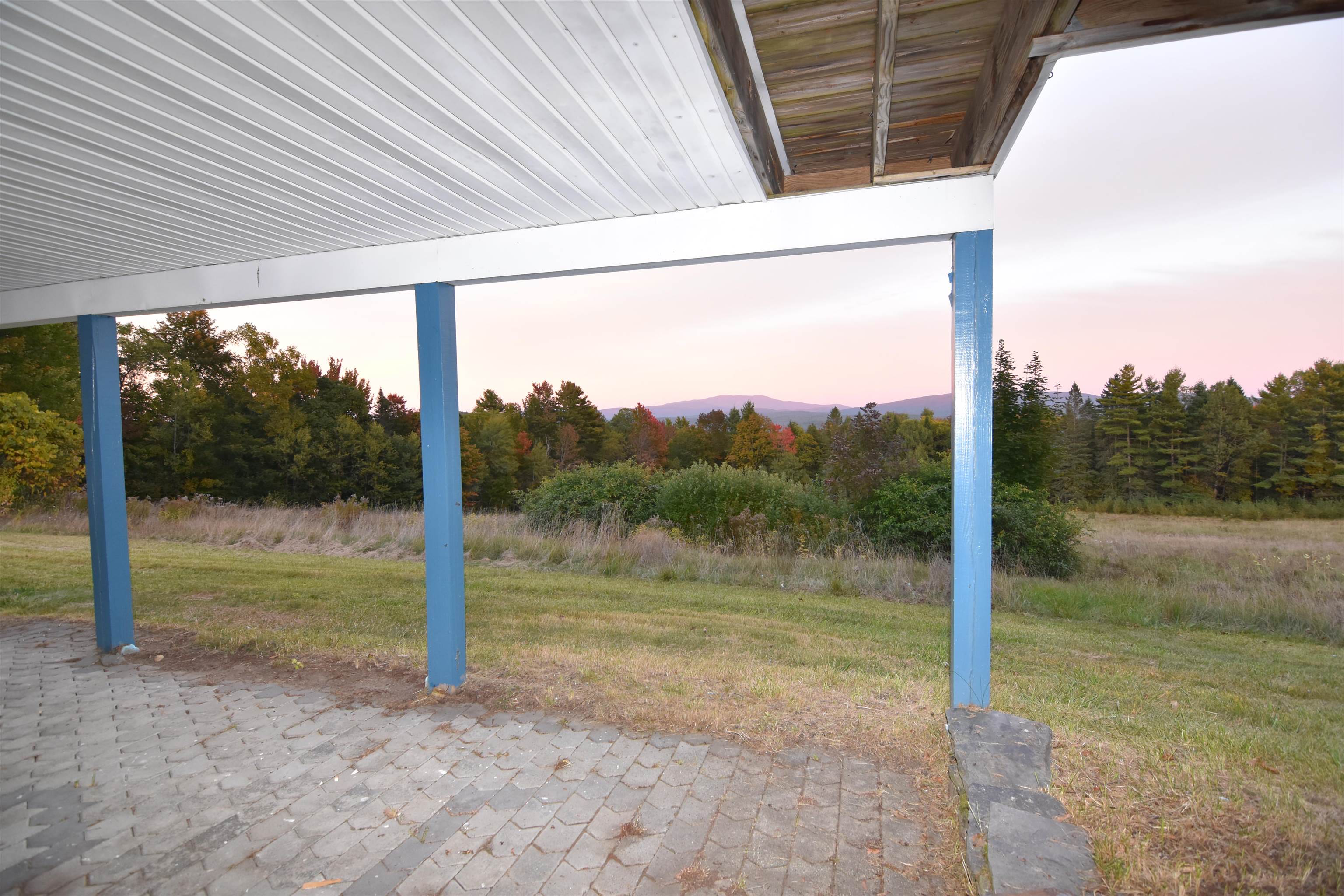 Covered patio overlooks an autumn yard, forest, and distant mountains beneath a pink dusk sky.