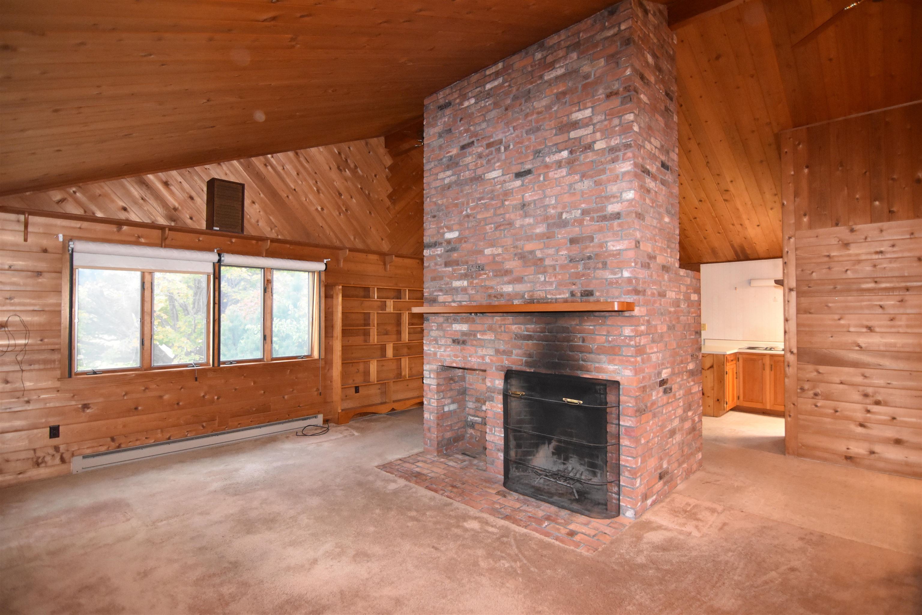 Wood-paneled living room with a vaulted ceiling and prominent brick fireplace beside built-in shelves.