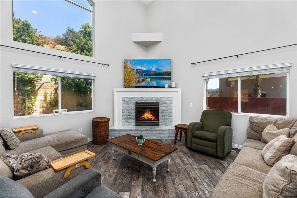 Living room with a vaulted ceiling, large windows, and a lit fireplace.
