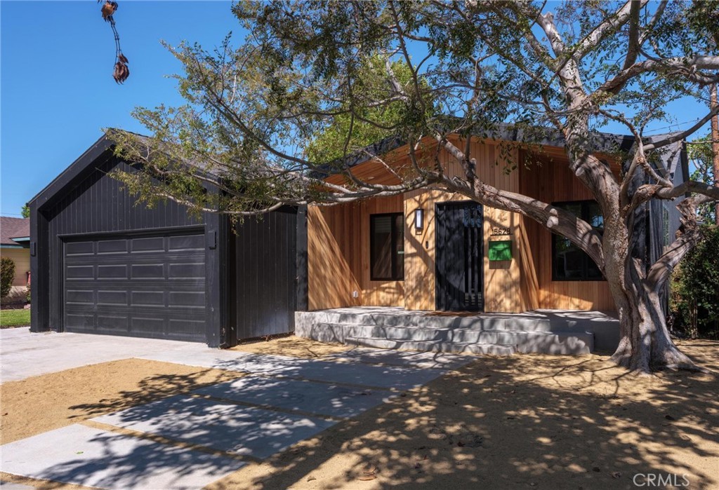 15628 Yukon home with wood siding, a black garage, and a large shade tree.