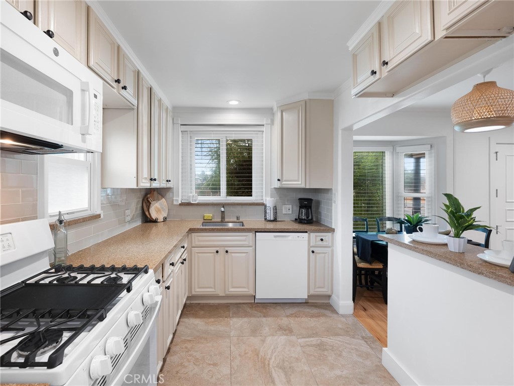 Bright white kitchen with gas range, tan counters, and a breakfast bar opening to a dining area.