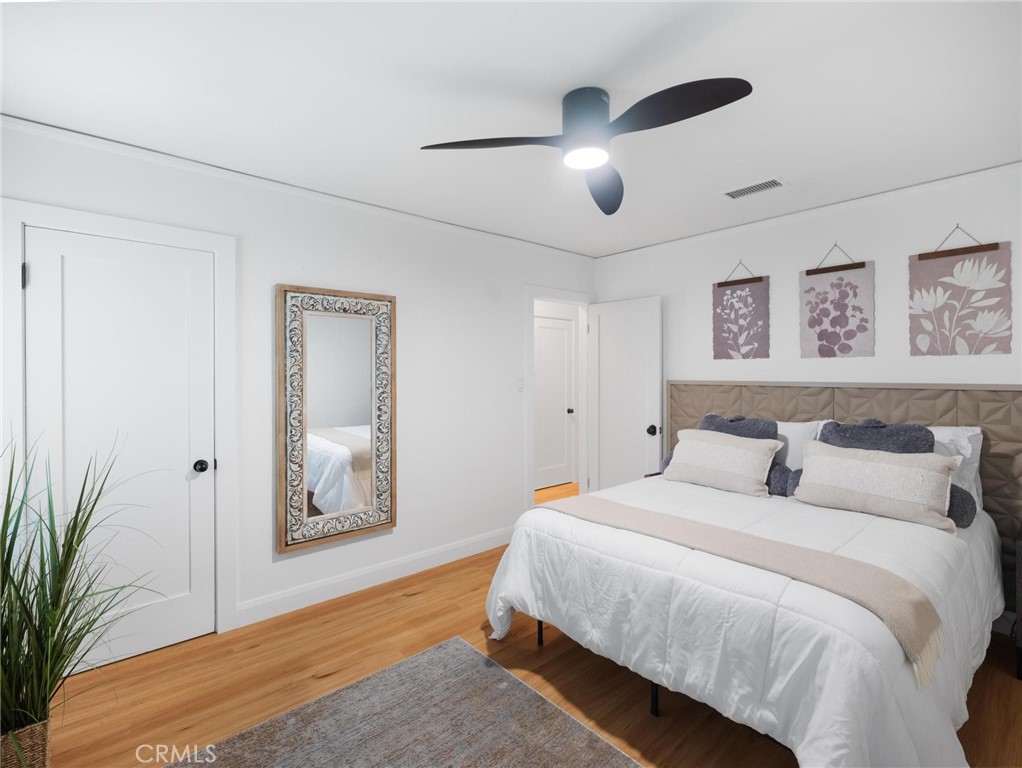 Furnished bedroom with a geometric upholstered headboard, botanical prints, and a dark ceiling fan.