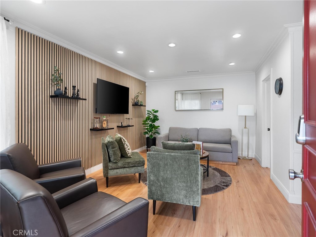 Living room with wood-slat television wall, gray sofa, green chairs, and light wood flooring.