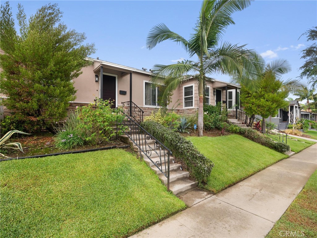 Single-story home with front steps, a green lawn, and palm trees.