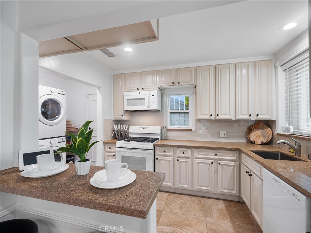 Kitchen with cream cabinets, granite counters, a breakfast peninsula, and a stacked washer and dryer.