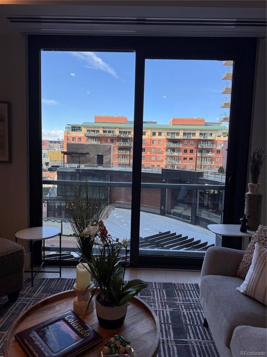 Furnished living room with a floor-to-ceiling window overlooking nearby buildings.