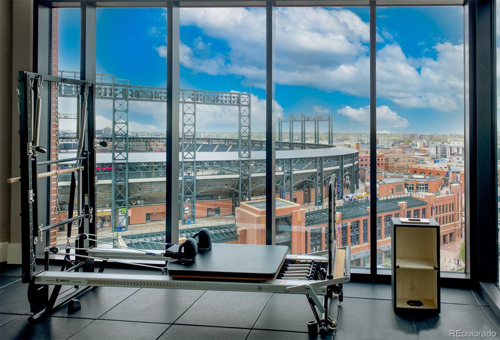 Fitness room with Pilates reformers and large windows overlooking a baseball stadium and downtown buildings.