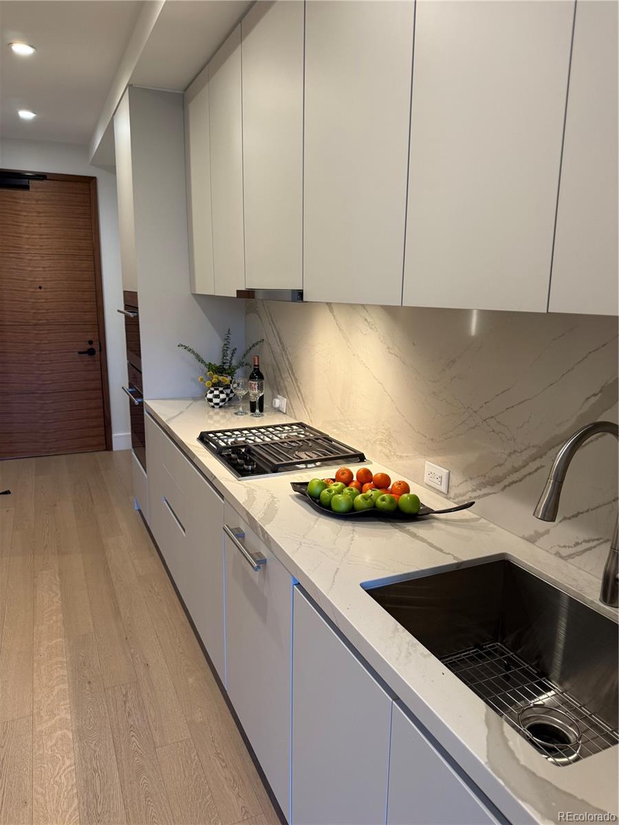Modern galley kitchen with white cabinets, veined stone counters, a gas cooktop, and a deep stainless steel sink.
