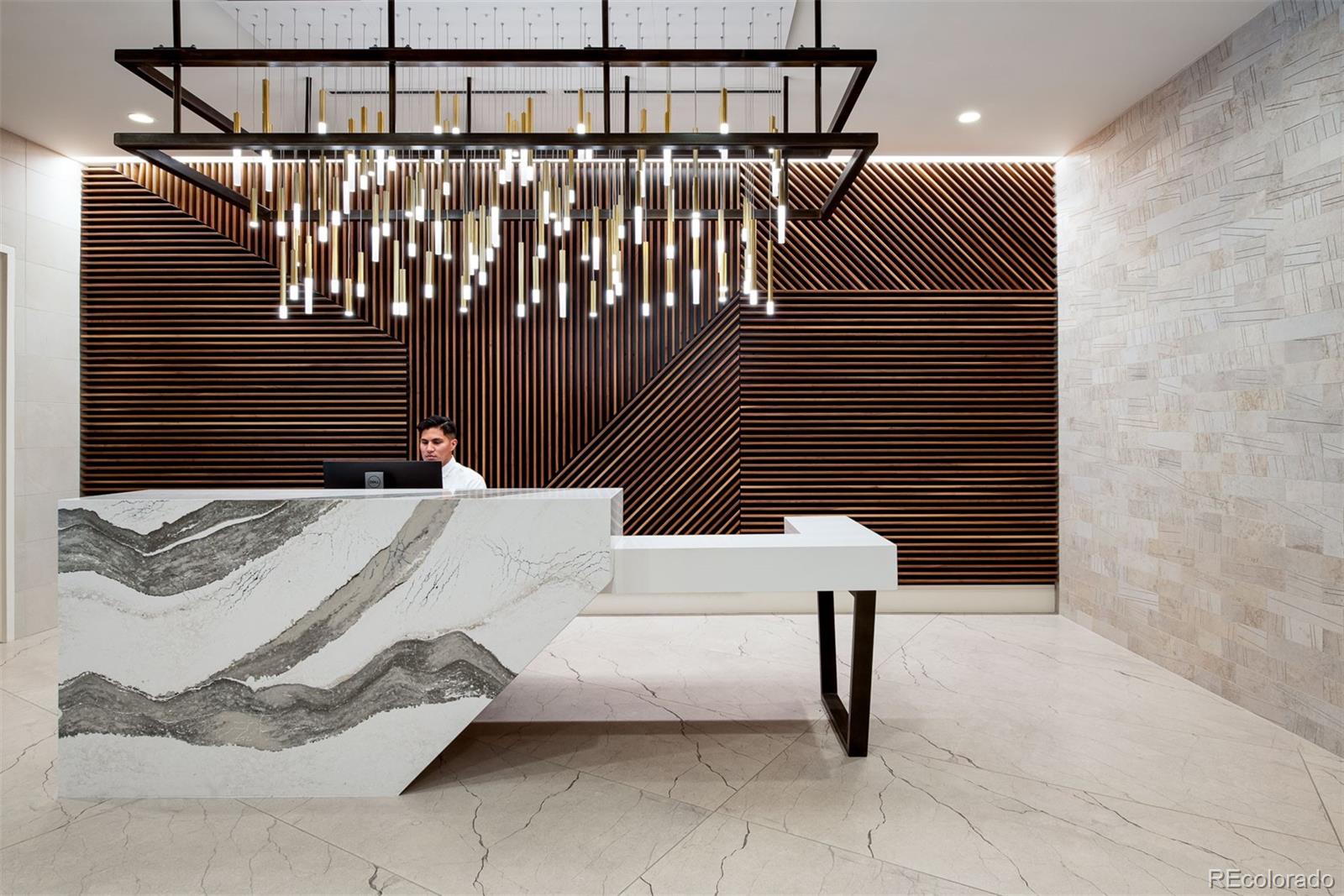 Building lobby reception desk with a dramatic wood-slat wall and suspended lights.