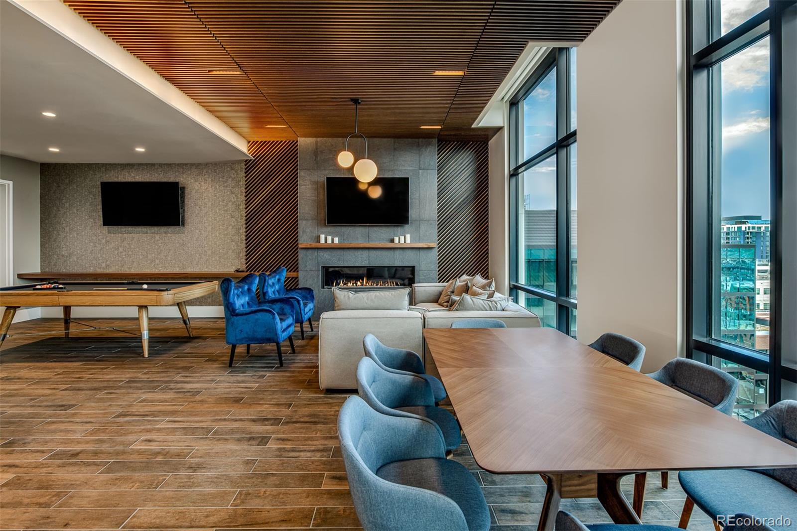 Furnished lounge with a fireplace, pool table, and dining table beside tall windows.