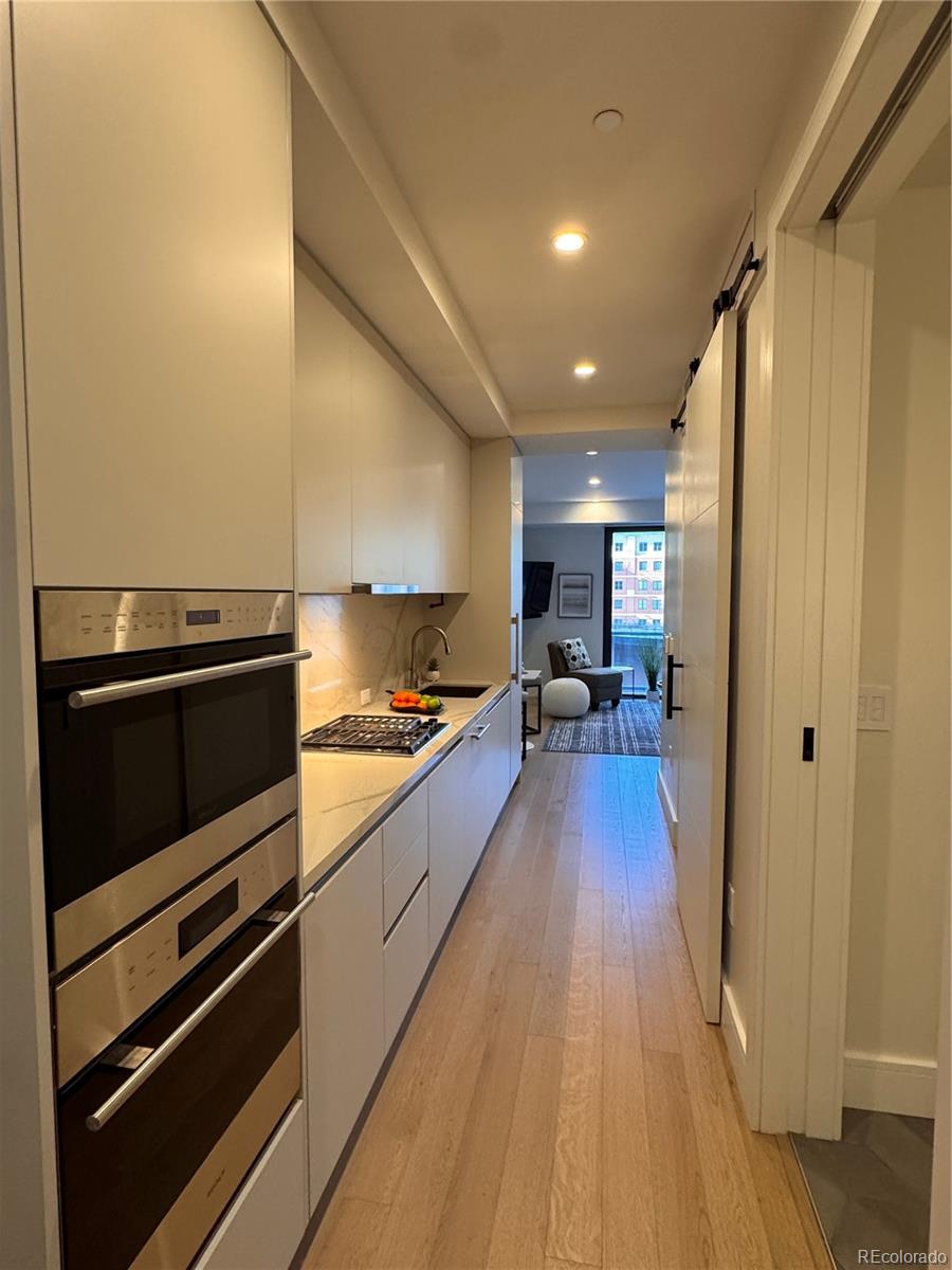 Modern galley kitchen with white cabinets, stainless steel double ovens, and a gas cooktop.
