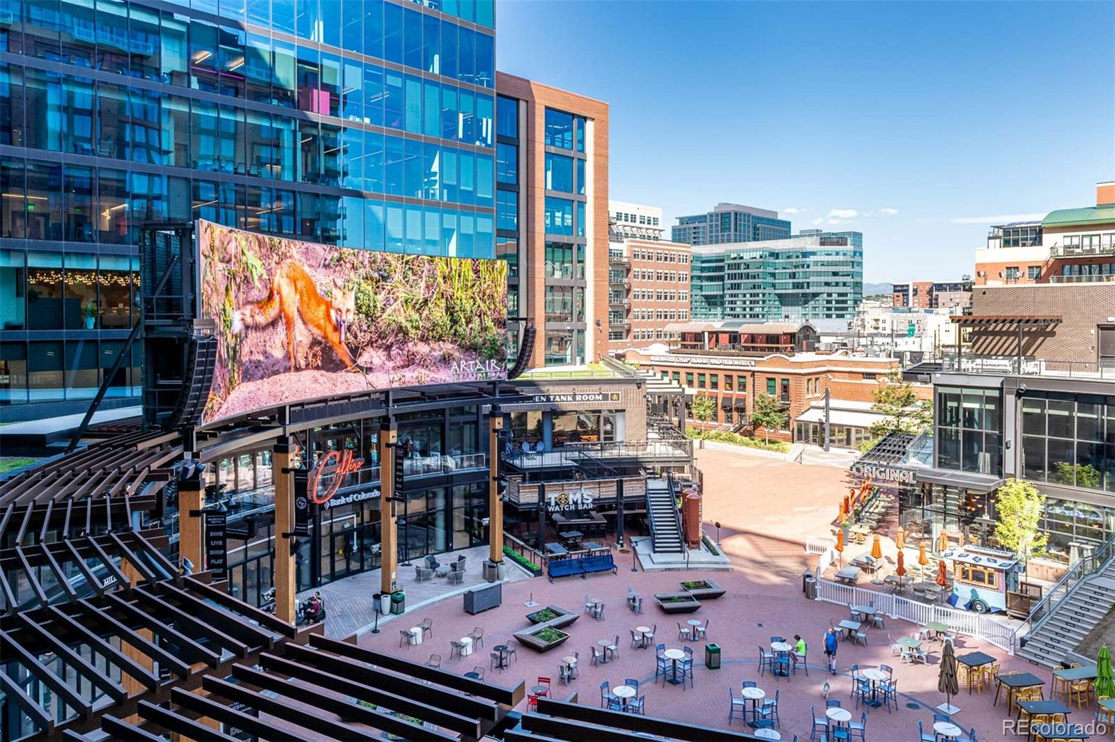 Downtown plaza with outdoor seating, restaurant patios, and modern glass and brick buildings.