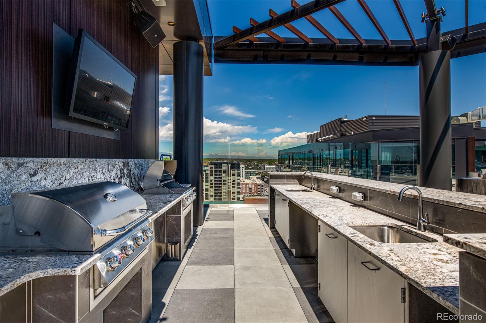 Rooftop outdoor kitchen with a stainless steel grill, stone counters, and downtown views.