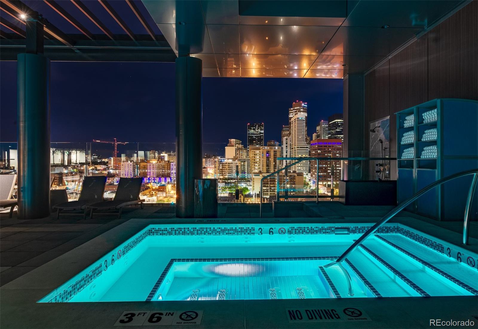 Rooftop pool glows beneath the Denver skyline at night, with lounge chairs beside the water.