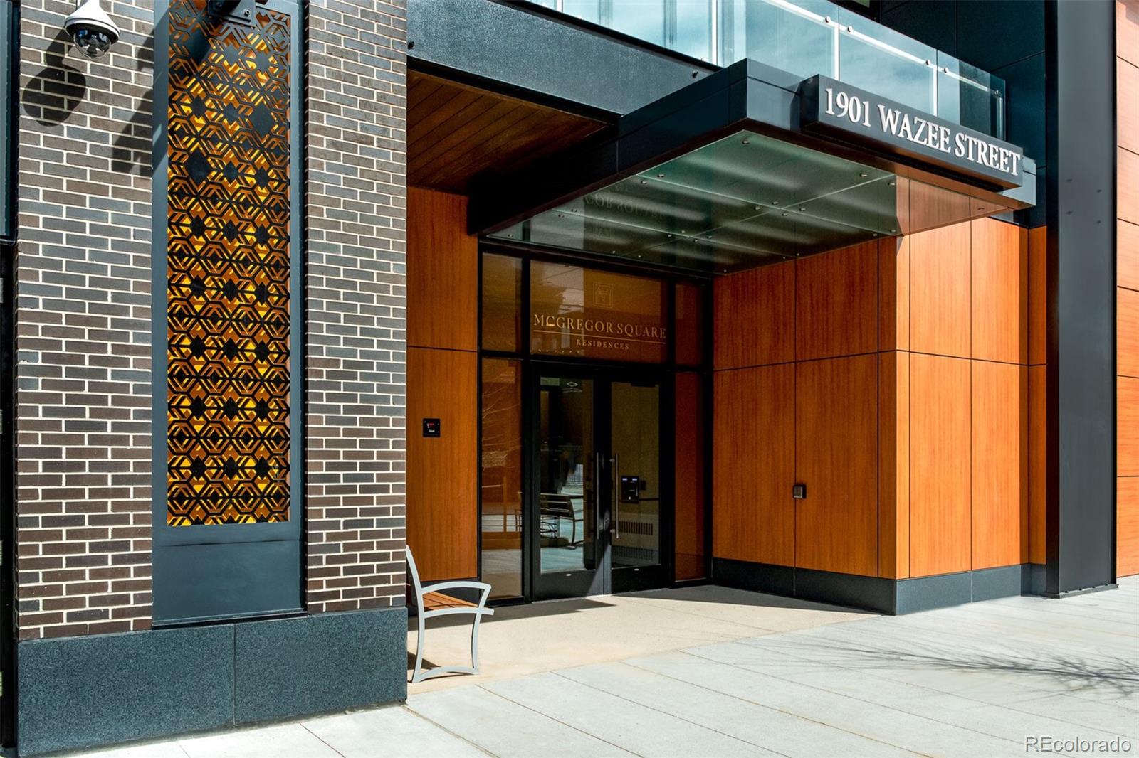 McGregor Square Residences entrance with a glass canopy, warm wood paneling, and decorative brickwork.