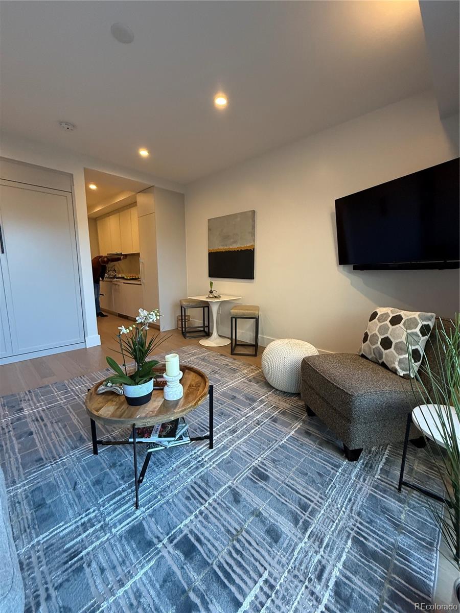 Furnished living room with a patterned rug, round wood coffee table, sofa, and wall-mounted television.