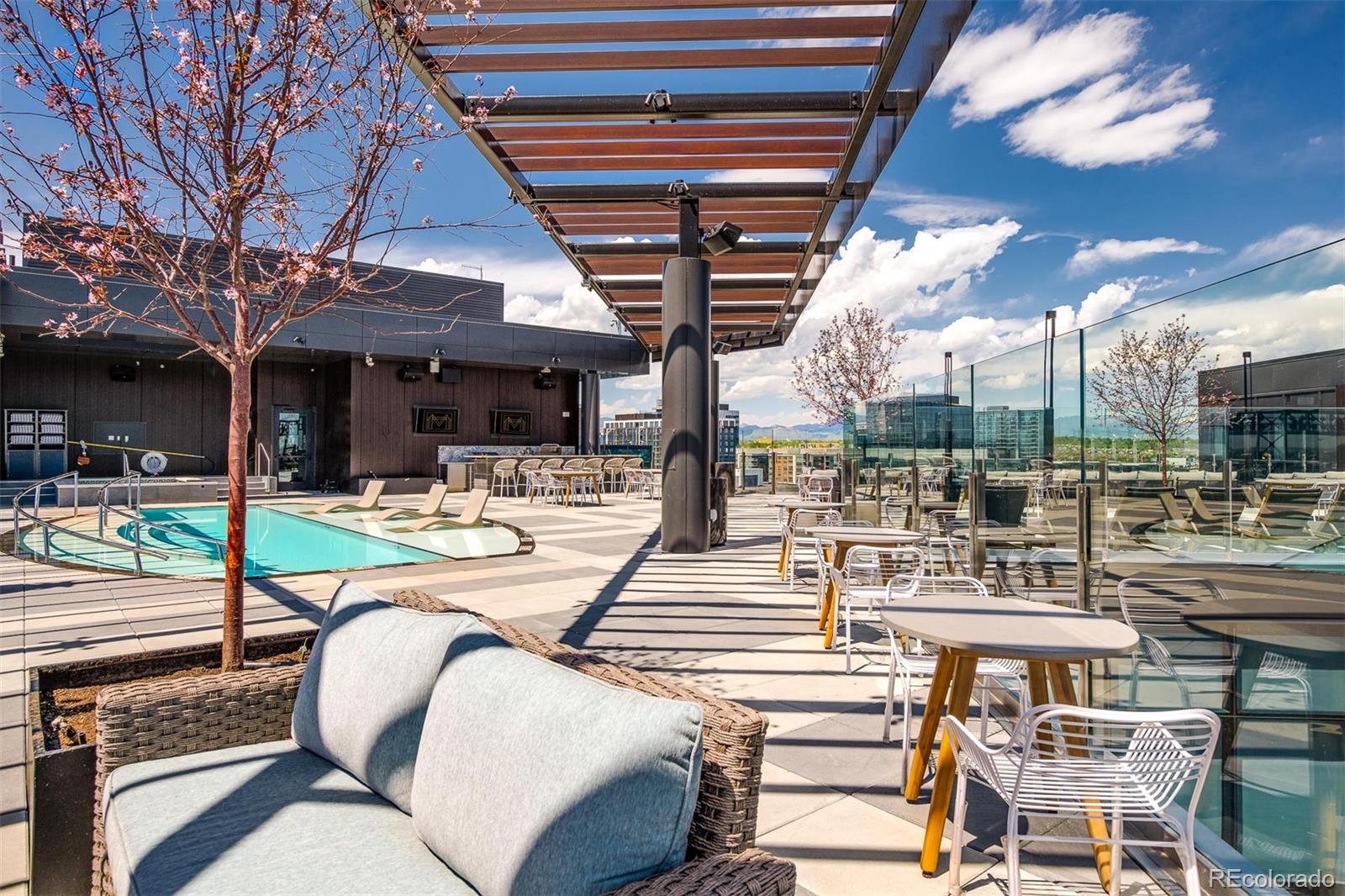 Rooftop pool terrace with lounge chairs, dining tables, glass railings, and distant mountain views.
