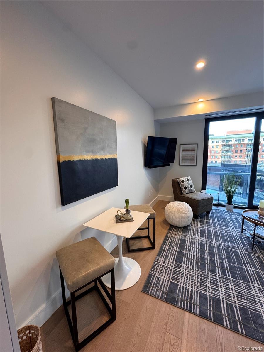 Furnished living room with abstract wall art, a geometric rug, and large windows overlooking neighboring buildings.