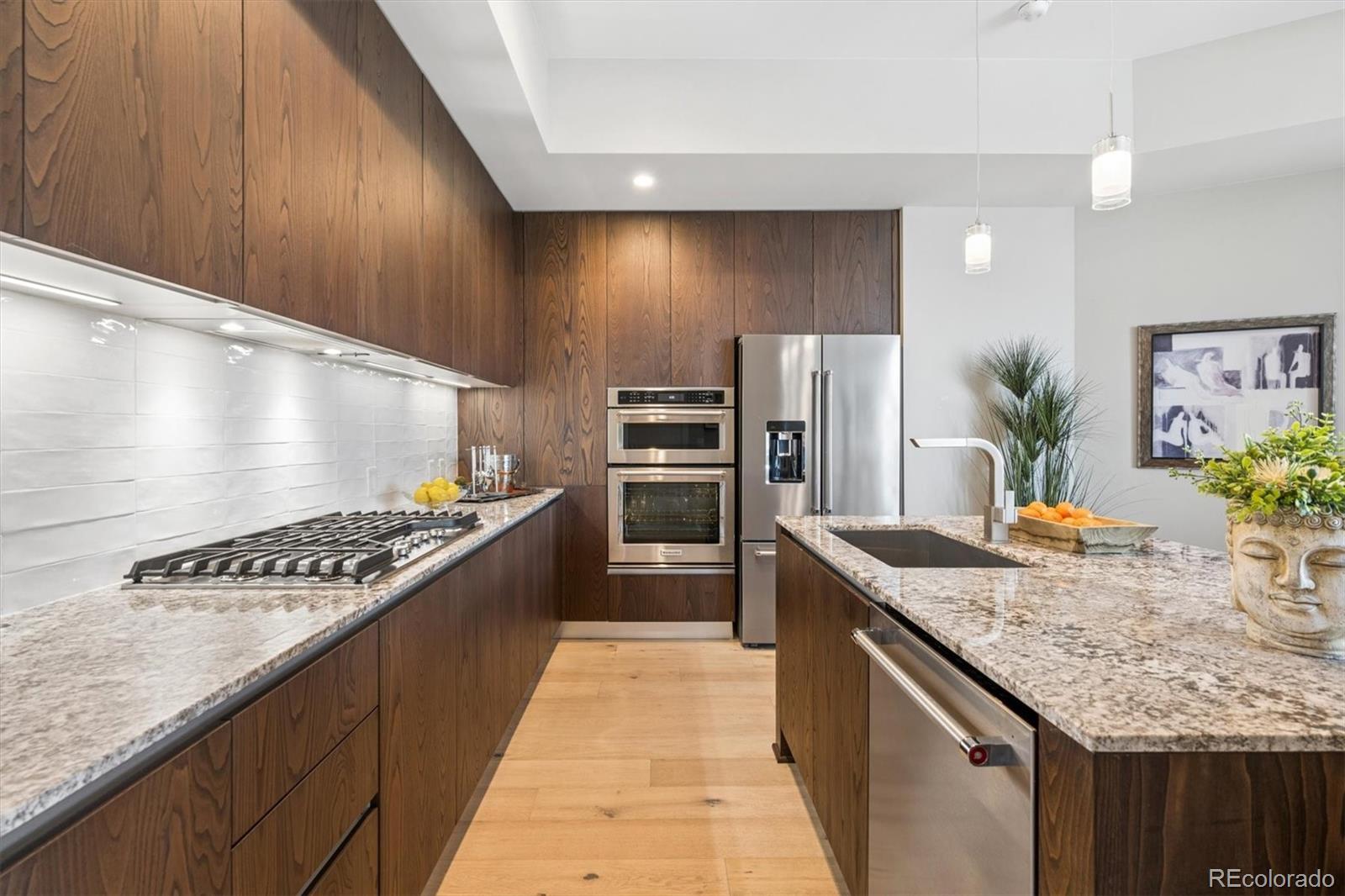 Modern kitchen with dark wood cabinets, granite counters, stainless steel appliances, and a sink island.
