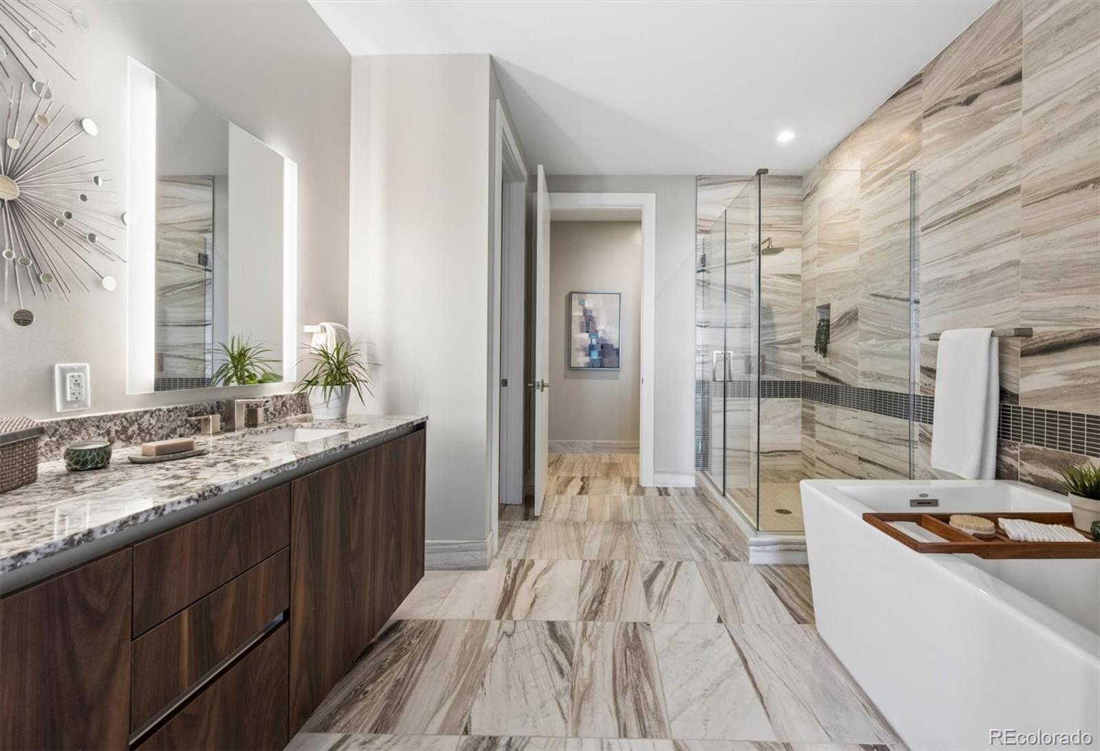 Bathroom with a glass shower, freestanding tub, marble-look tile, and dark wood vanity.