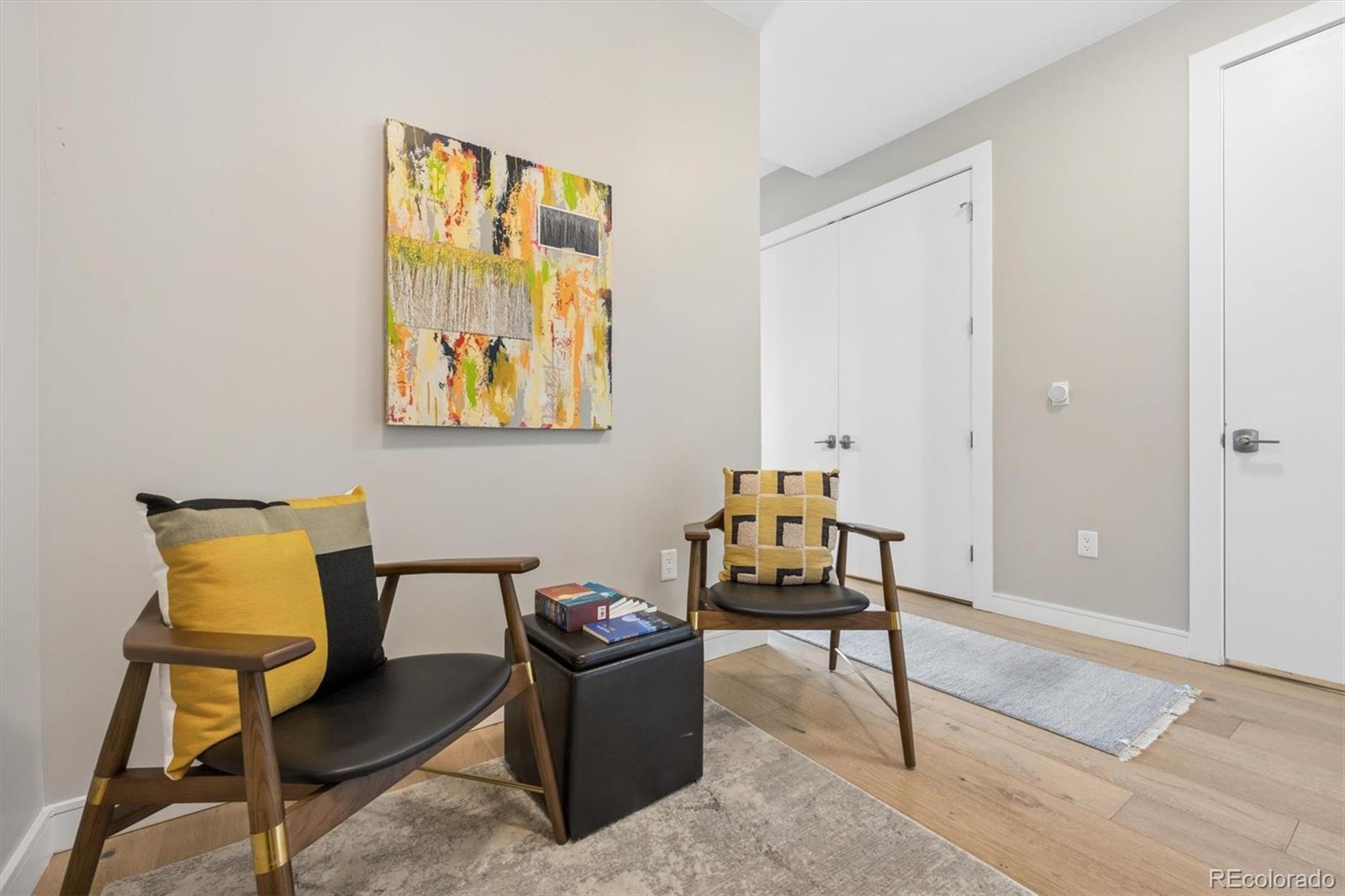 Staged living room seating area with modern chairs, colorful abstract art, and light wood flooring.