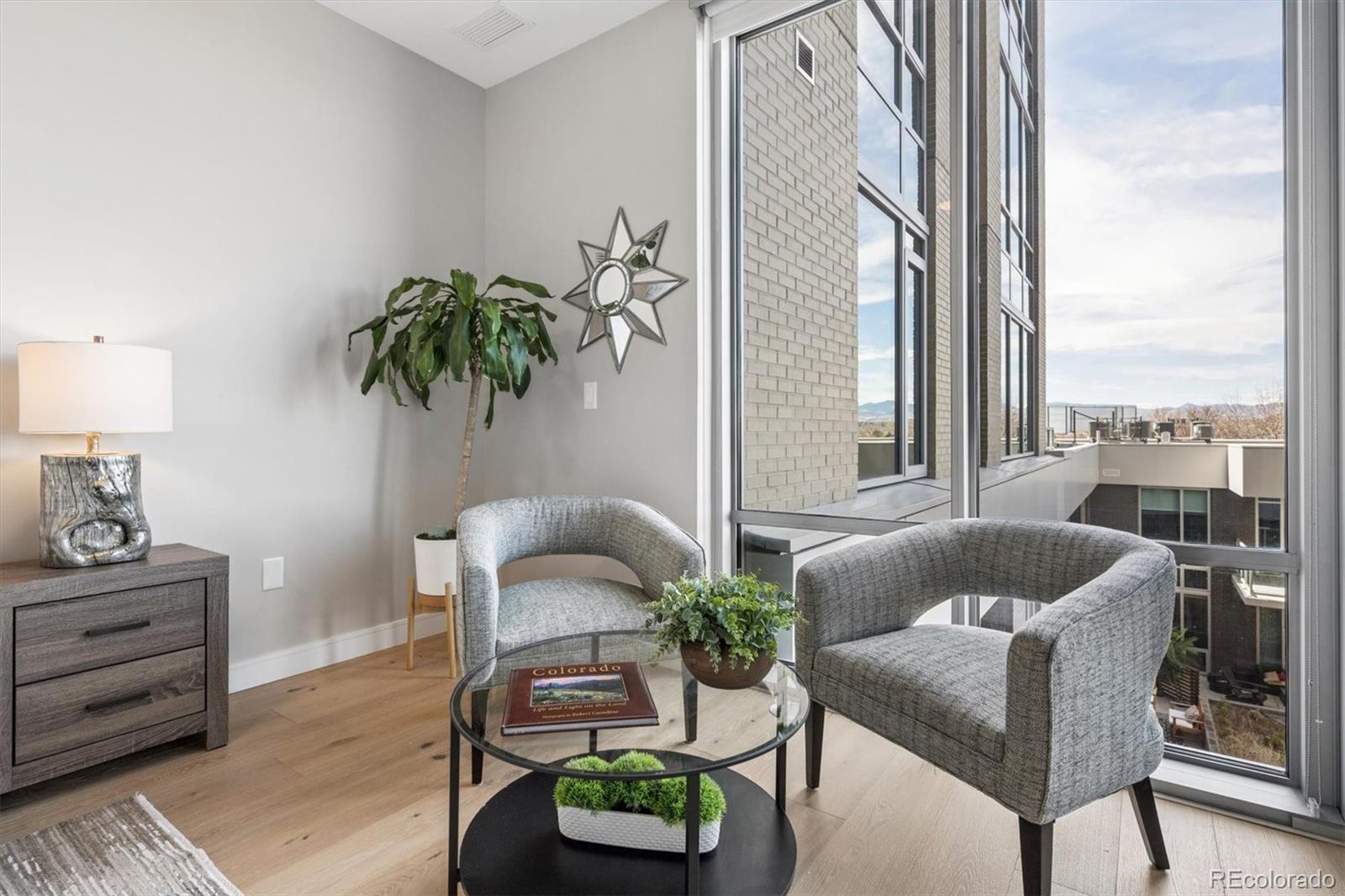 Furnished living room with gray armchairs and floor-to-ceiling windows overlooking the city.
