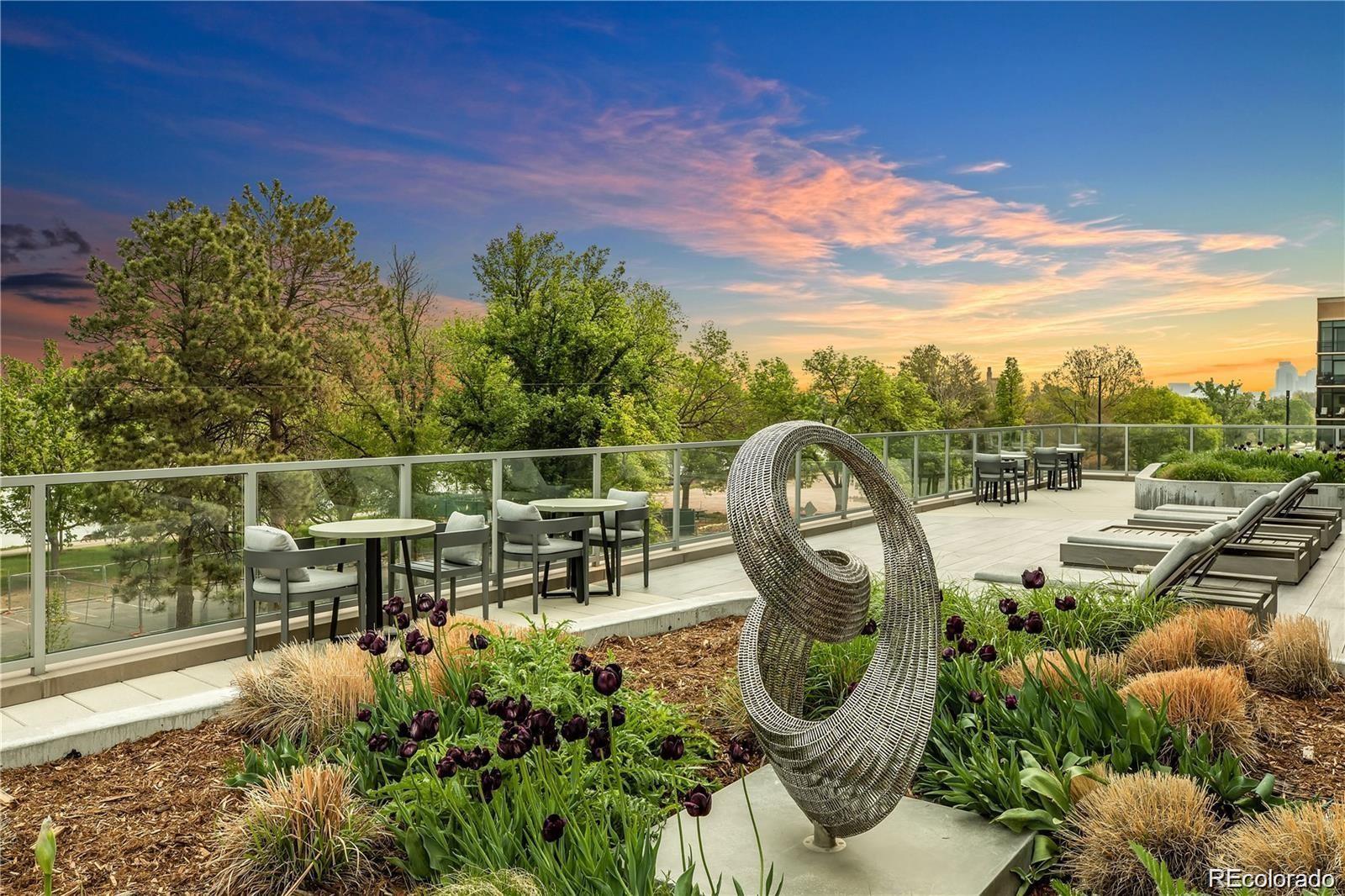 Rooftop terrace with dining tables, lounge chairs, a sculptural metal installation, and sunset views.