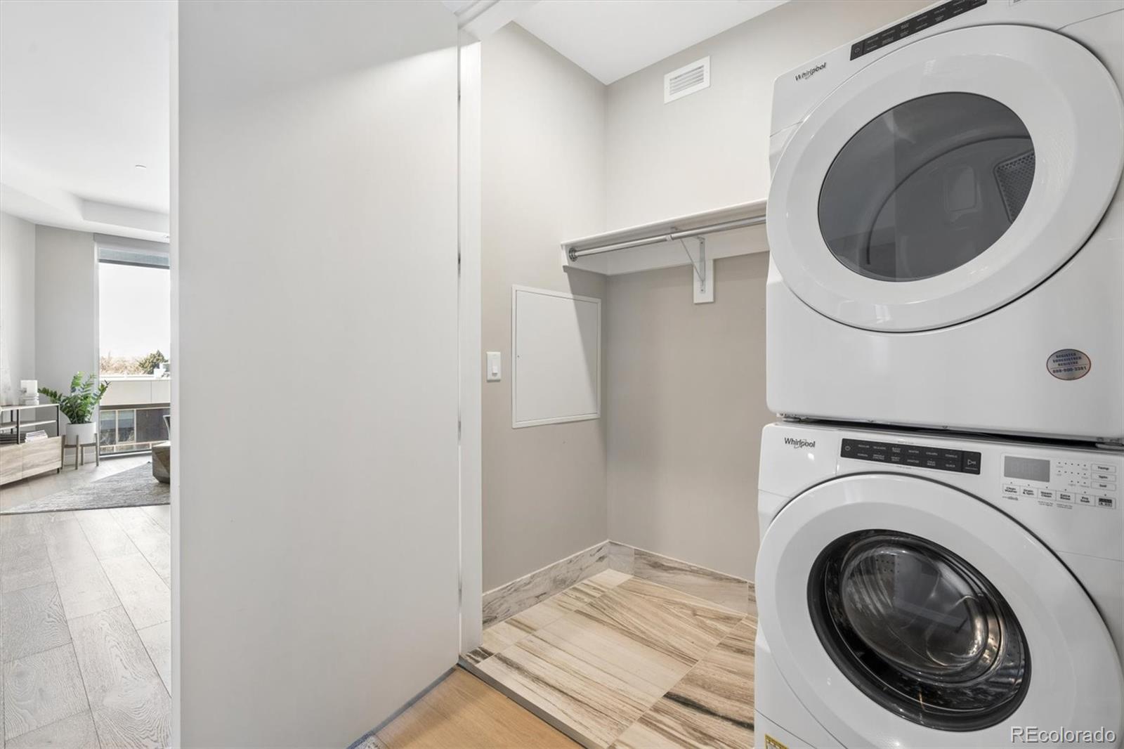 Condo laundry area with stacked Whirlpool washer and dryer beside a hanging rod.