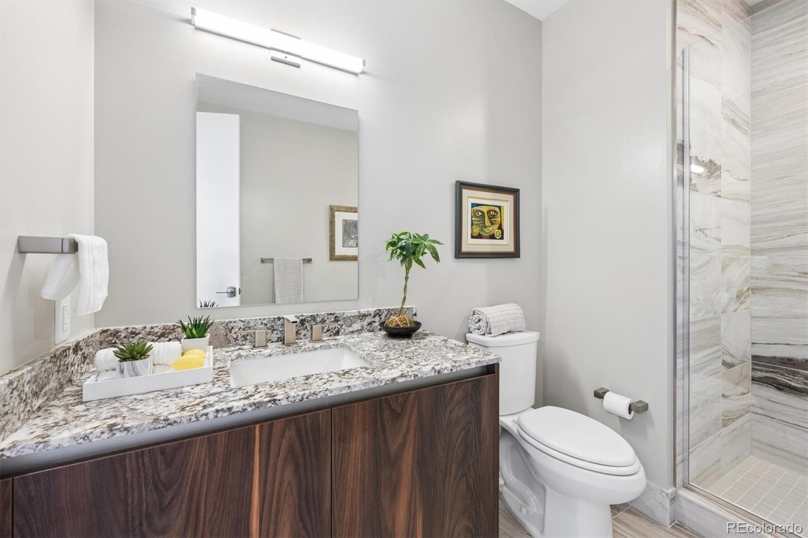 Bathroom with a speckled granite vanity and glass shower clad in pale marble-look tile.