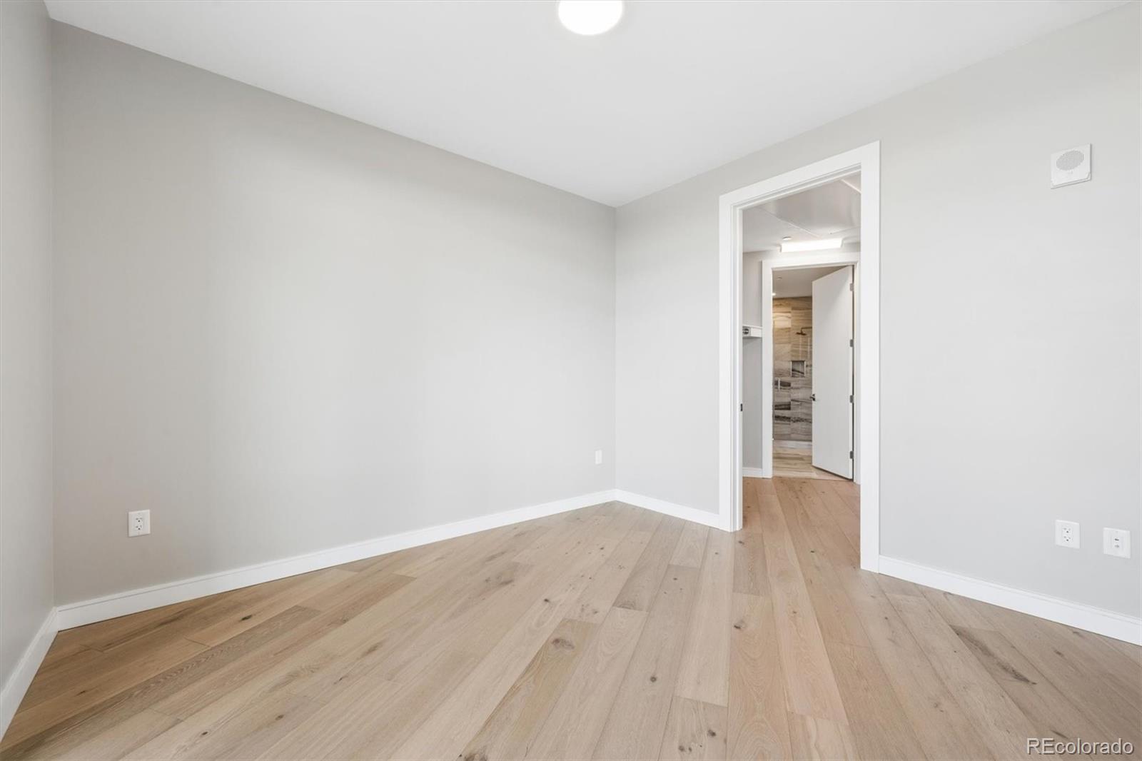 Empty room with light wood floors and an open doorway toward a tiled bathroom.