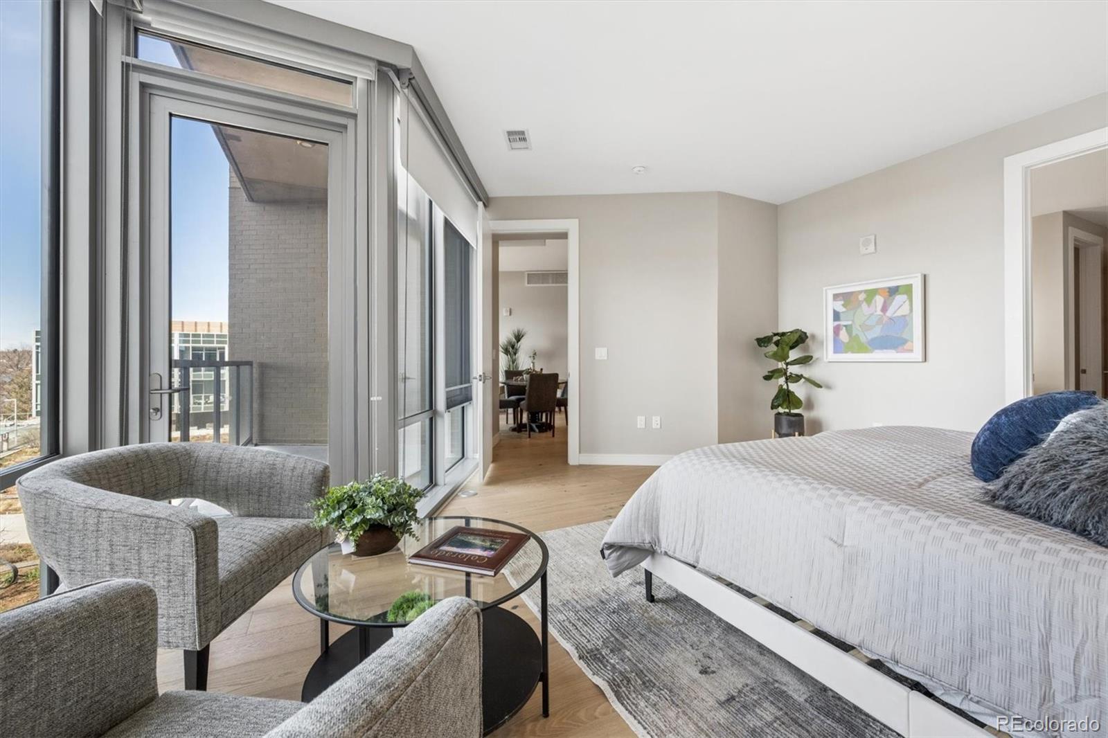 Furnished bedroom with floor-to-ceiling windows, a balcony, and a sitting area.