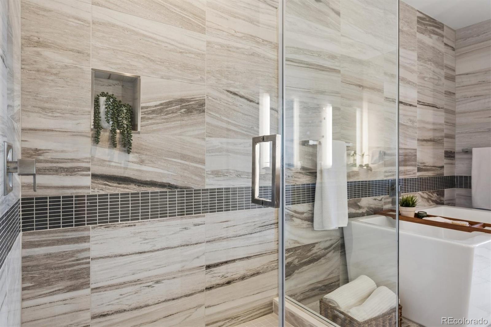 Bathroom with a glass shower, white bathtub, veined tile walls, and a recessed plant niche.