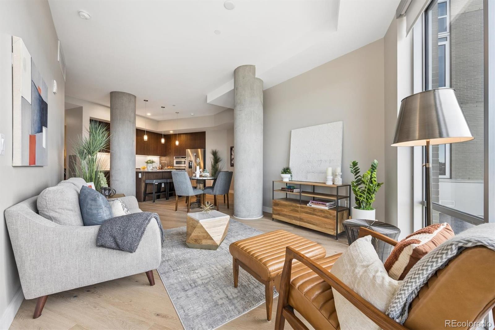 Open-plan living room with concrete columns, leather chairs, and a kitchen and dining area beyond.