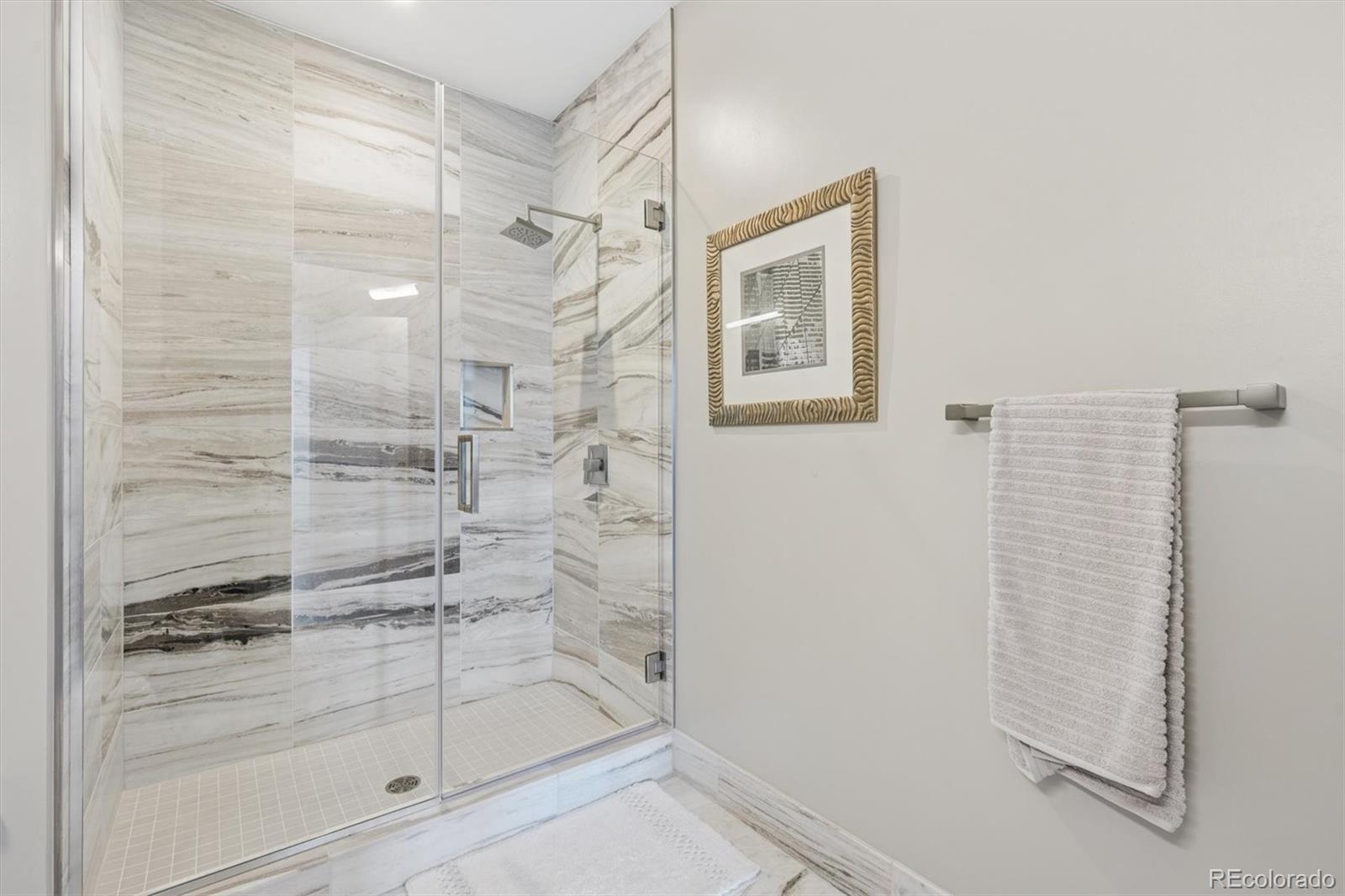 Walk-in shower with veined stone tile, glass doors, rainfall showerhead, and recessed niche.