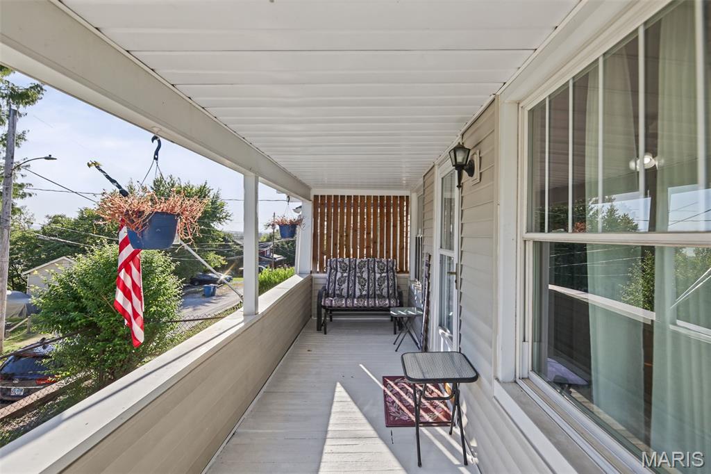 Covered porch with a cushioned loveseat, hanging flower baskets, and windows along the house.