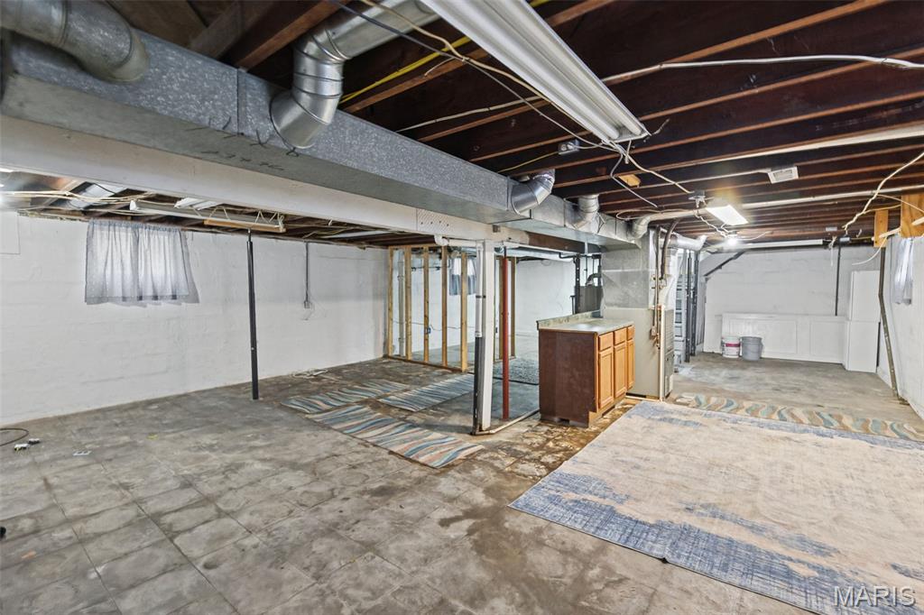 Unfinished basement with exposed joists and ductwork, open wall framing, and rugs on the concrete floor.