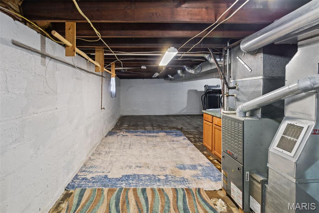 Unfinished basement with exposed joists, rugs on the concrete floor, and prominent furnace ductwork.
