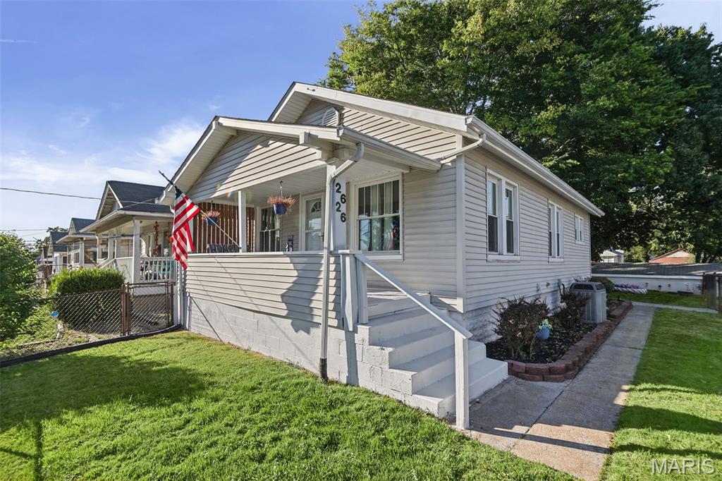 Single-story light-colored home with a covered porch, front steps, American flag and green lawn.