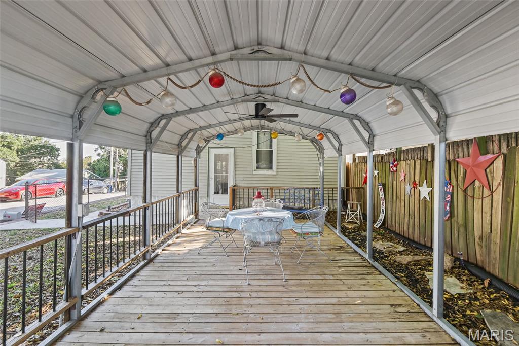 Covered wooden deck with outdoor dining set, colorful string lights, and a decorated fence.