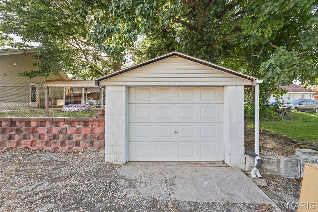 White detached garage with a paneled door, concrete driveway, and mature trees.