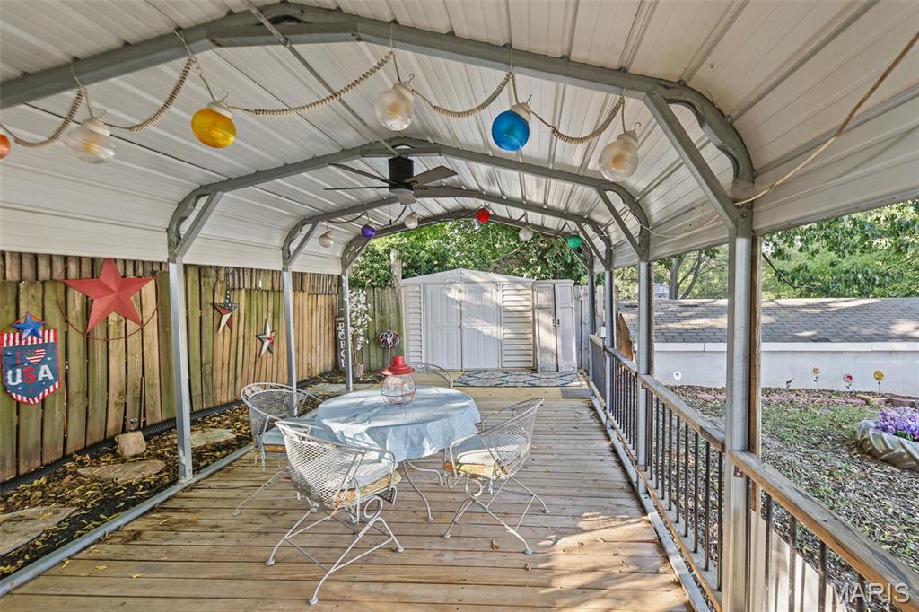 Covered wooden deck with a round dining set, string lights, and a white storage shed.