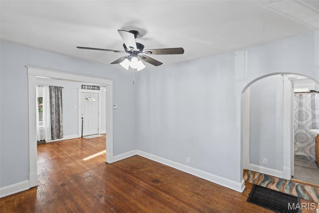 Empty room with hardwood floors, a ceiling fan, and an arched doorway to the bathroom.